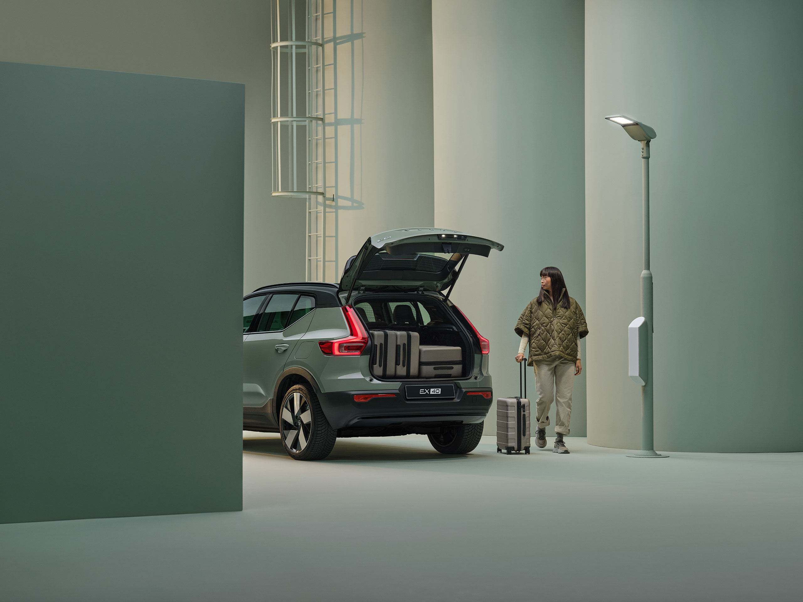 Volvo EX40 สีเขียวอมเทาพร้อมประตูท้ายที่เปิดอยู่ และมีกระเป๋าเดินทางอยู่ด้านใน