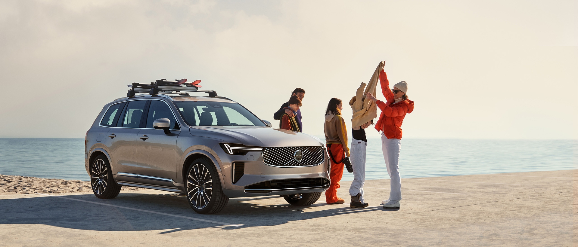 A family at the beach near a Volvo XC90 Plug-in hybrid, changing from skiing clothes to swimming clothes.