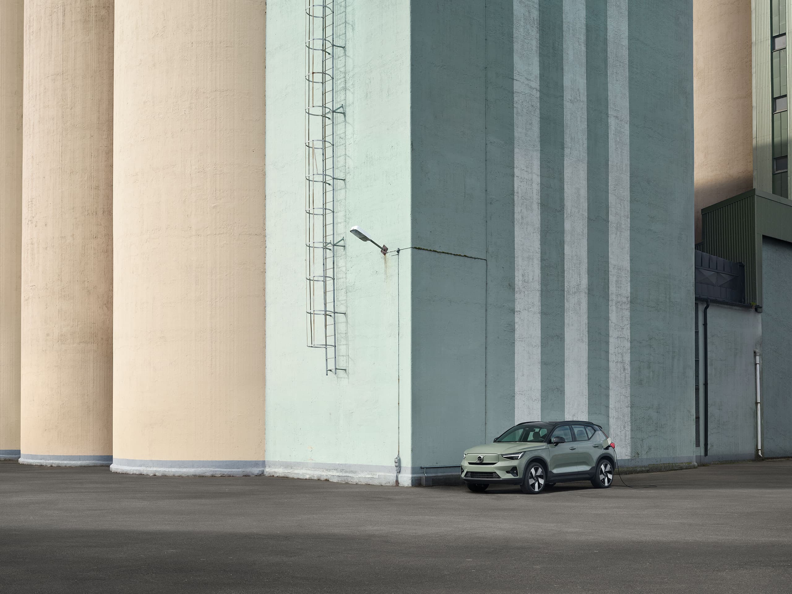 Volvo EX40 สีเขียวอมเทาจอดอยู่ข้างอาคารคอนกรีตขนาดใหญ่