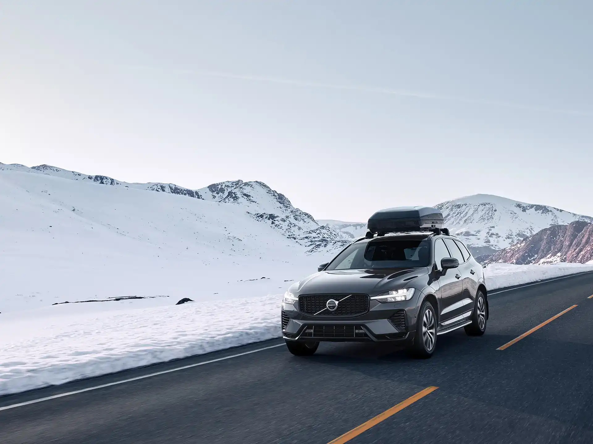 Ein Volvo XC60 mit Dachbox fährt durch verschneites Gelände.