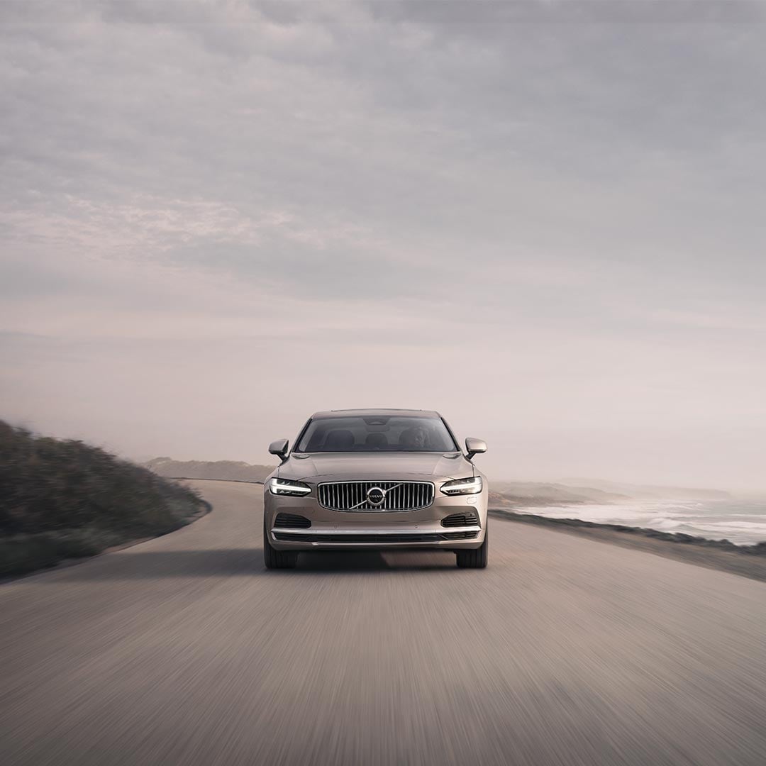 Image de l'avant d'une Volvo S90 roulant sur une route au bord de la mer.