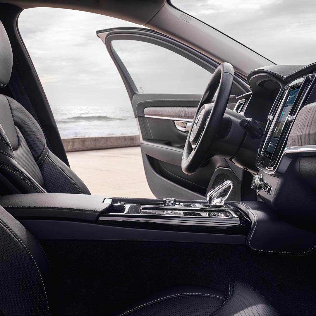 Innenansicht eines Volvo S90 Plug-in Hybrid mit Fahrersitz, Lenkrad, Schalthebel und zentralem Touchscreen-Display.