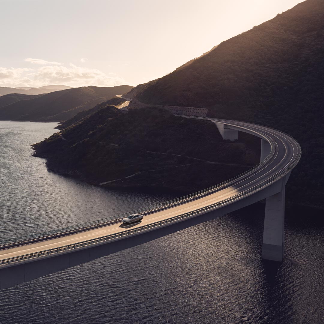 Weitwinkelaufnahme eines Volvo S90 Plug-in Hybrid, der über eine Brücke mit Blick auf einen Fluss und Berge fährt.