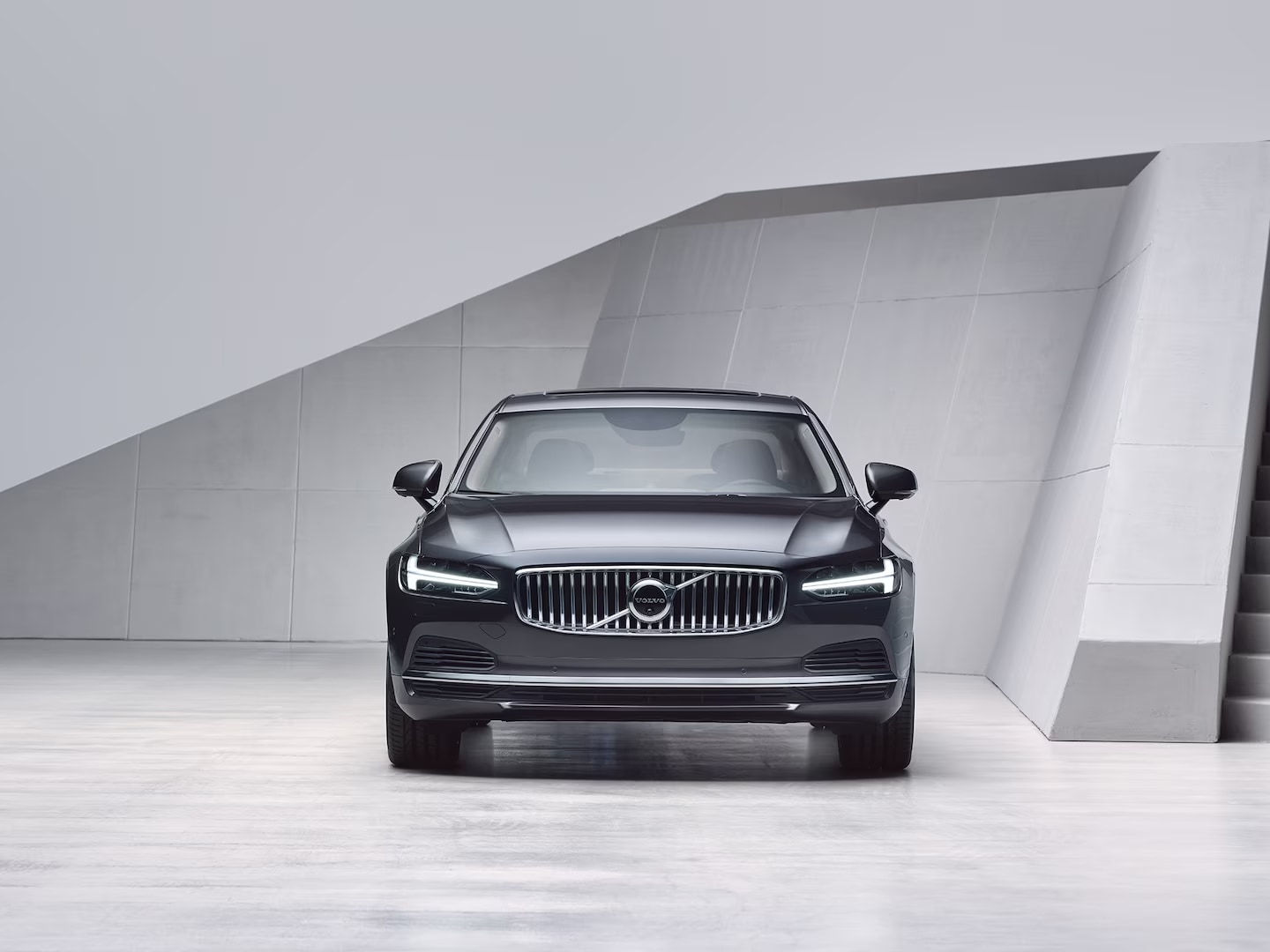 A Volvo S90 Recharge partially obscured by stairs.