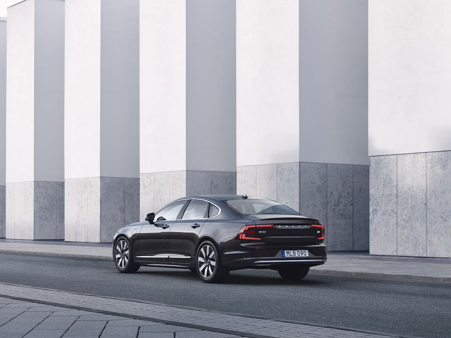 Volvo S90 Recharge seen from rear side in front of concrete wall.