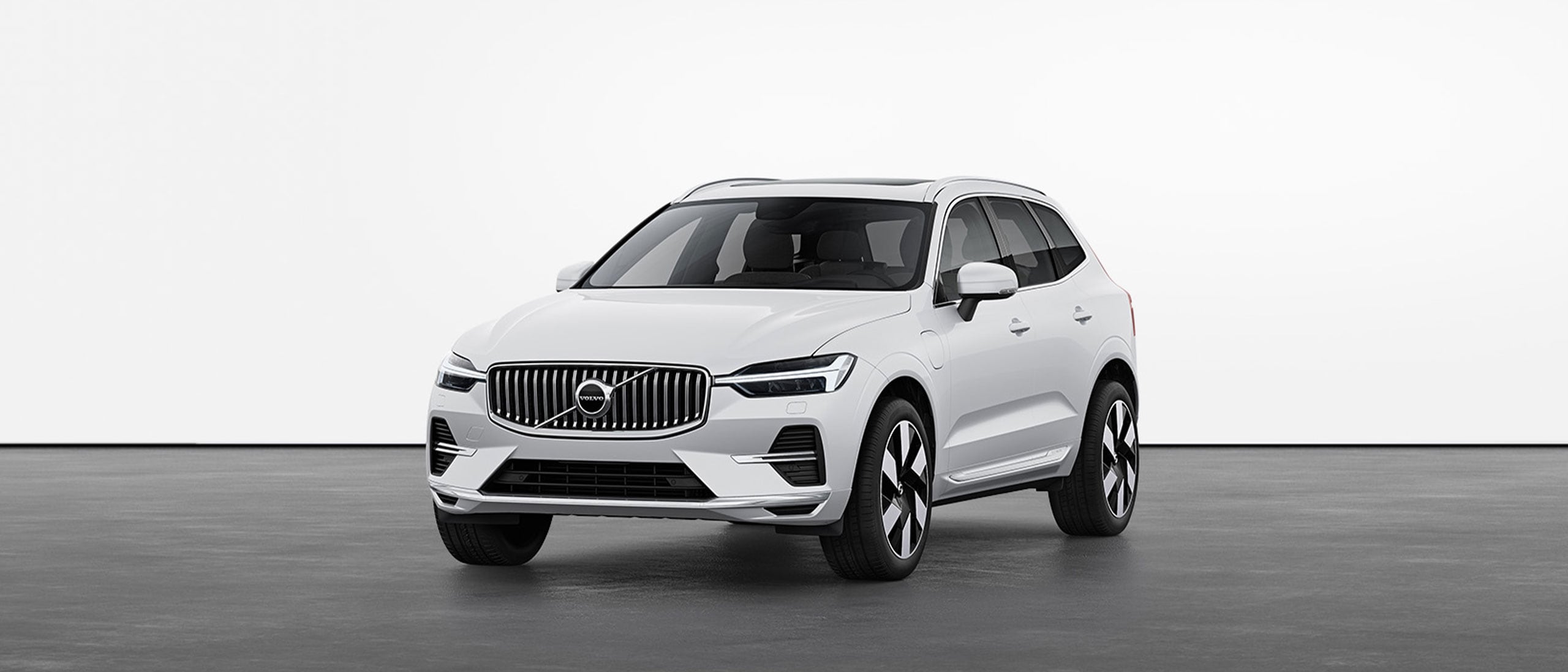 A white Volvo XC60 Recharge plug-in hybrid SUV standing still on grey floor in a studio.