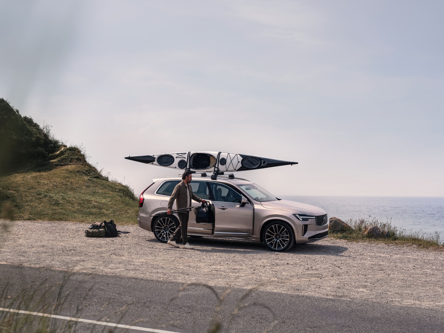 Imagen de estilo de vida de un hombre cargando en un Volvo XC90 híbrido enchufable un equipo de kayak.