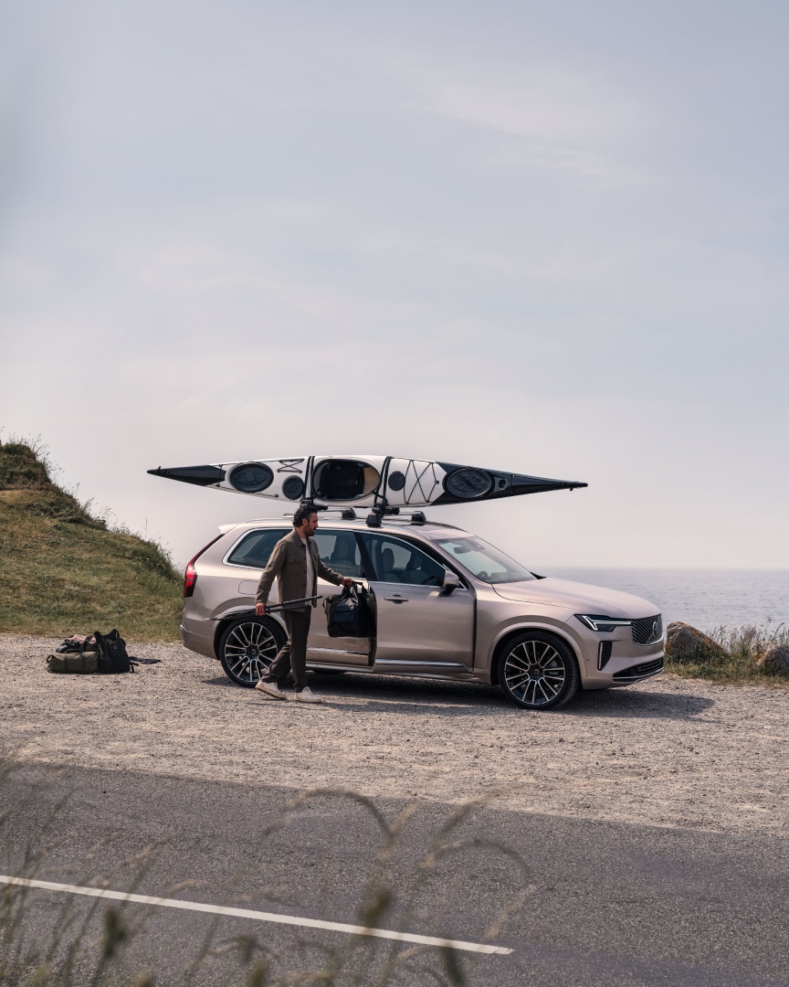 Imagen de estilo de vida de un hombre cargando en un Volvo XC90 híbrido enchufable un equipo de kayak.