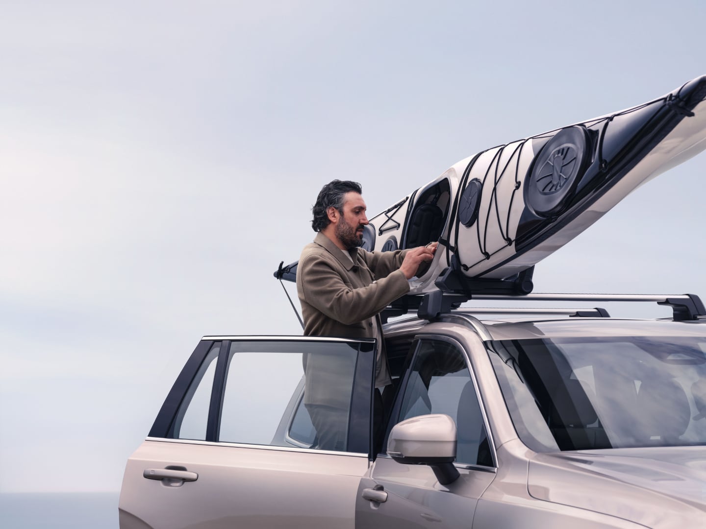 Imagen de estilo de vida de un hombre montando un kayak en el soporte del kayak en un Volvo XC90 híbrido enchufable.