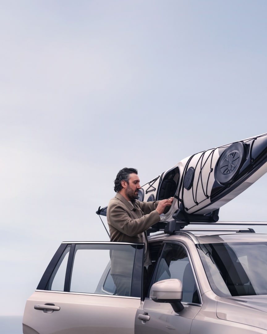 Imagen de estilo de vida de un hombre montando un kayak en el soporte del kayak en un Volvo XC90 híbrido enchufable.