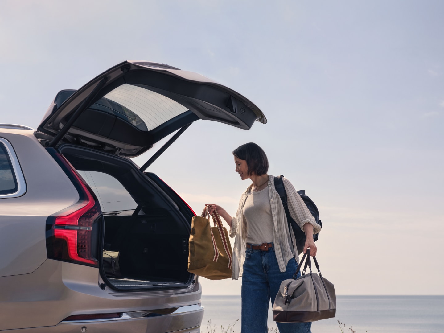 Lifestyle-Aufnahme einer Frau, die Taschen in den Laderaum eines Volvo XC90 Plug-in Hybrid stellt.