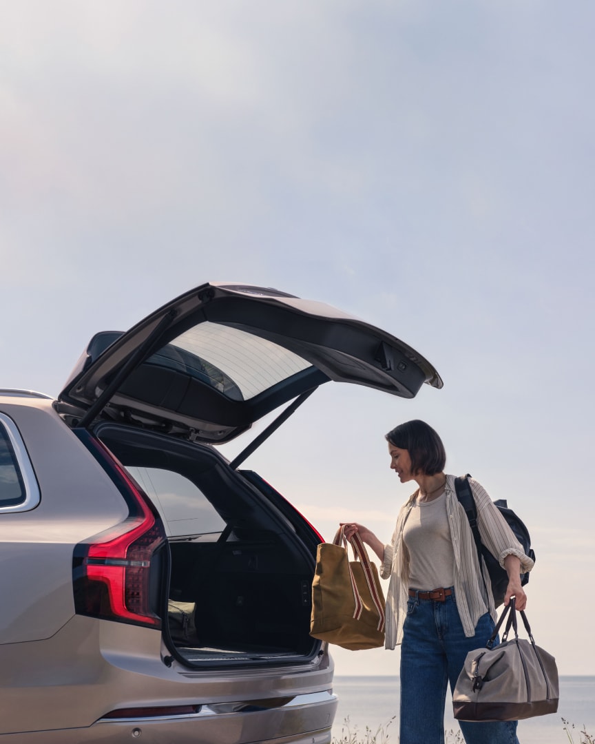 Imagen de estilo de vida de una mujer colocando bolsas en el compartimento de carga de un Volvo XC90 híbrido enchufable.