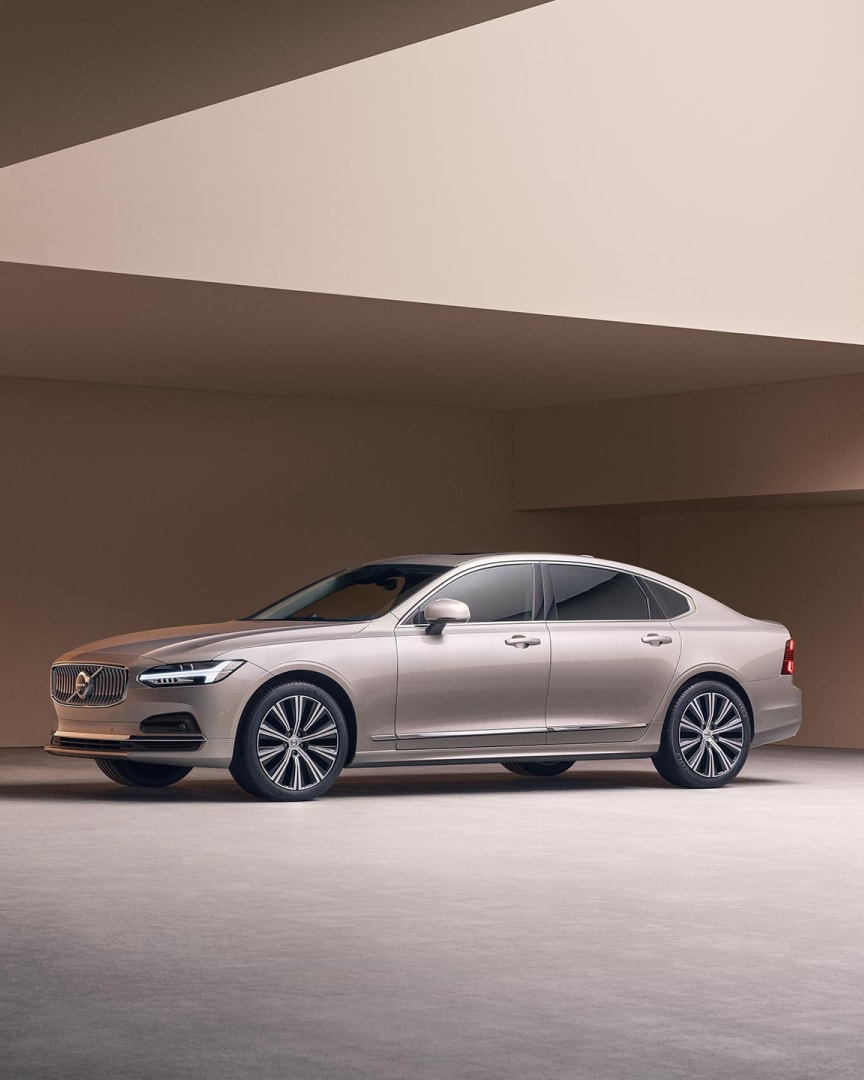 A wide-angle image of the left side and partial view of the front of a Volvo S90 parked in a large concrete structure.