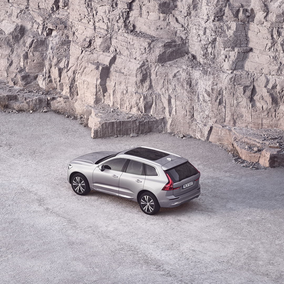 A silver Volvo XC60 with a panoramic roof next to a rock wall.