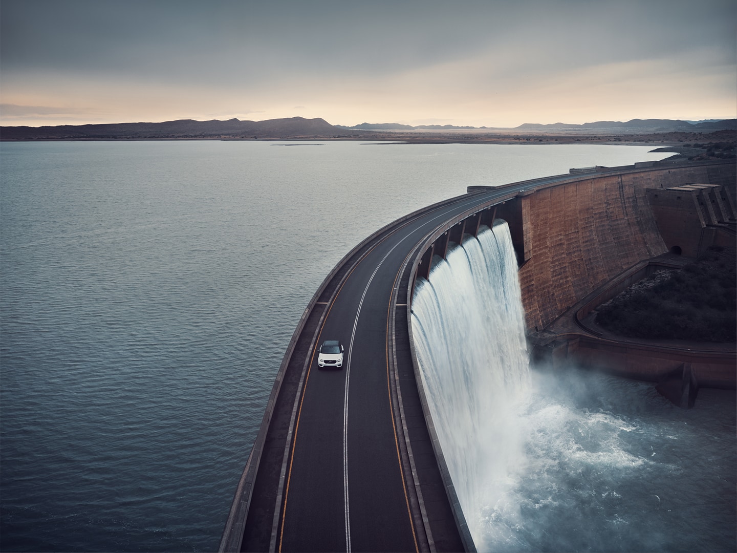 Un SUV Volvo circulando por una carretera sobre la presa de un embalse.