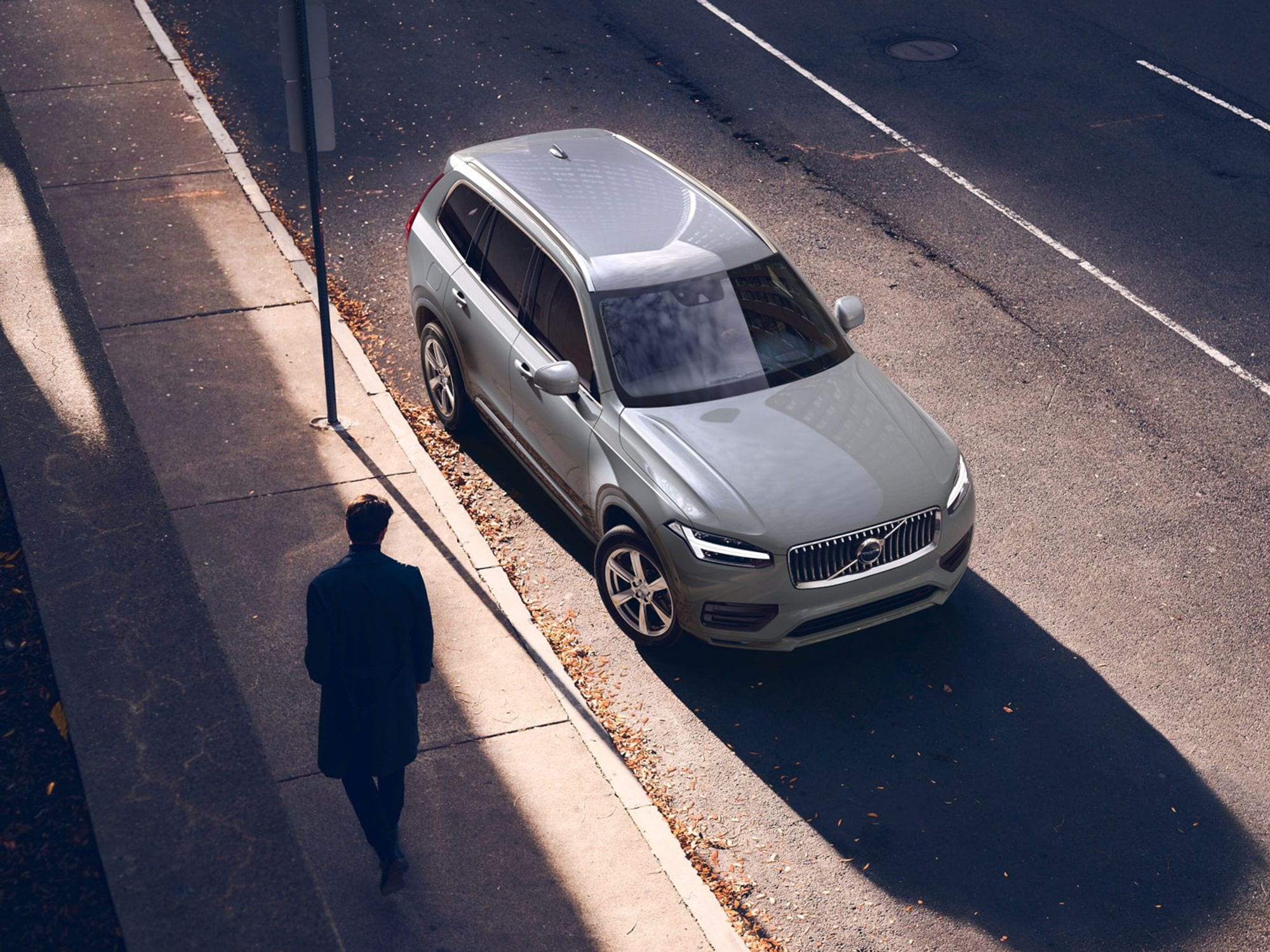 Silhouette van een persoon naast een Volvo XC90 geparkeerd langs de straat.