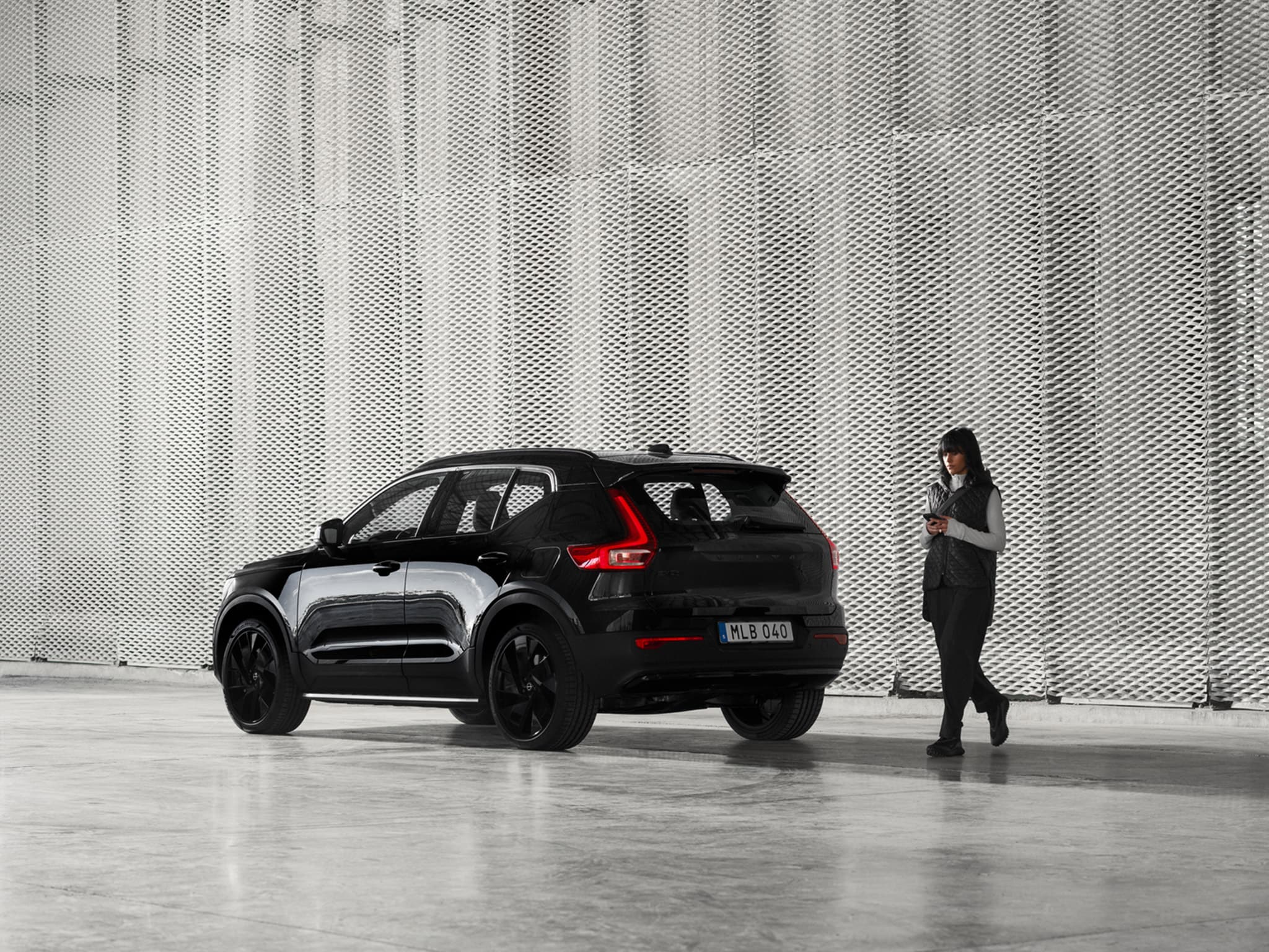 Nainen seisoo pysäköidyn Volvo EX40 Black Edition auton takana.