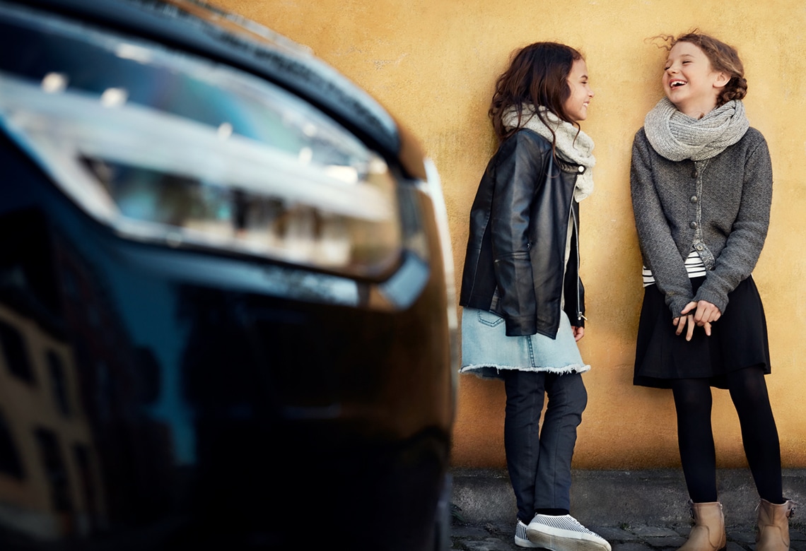 Lachende Kinder stehen neben einem Volvo an einer gelben Wand - Seitenschuss