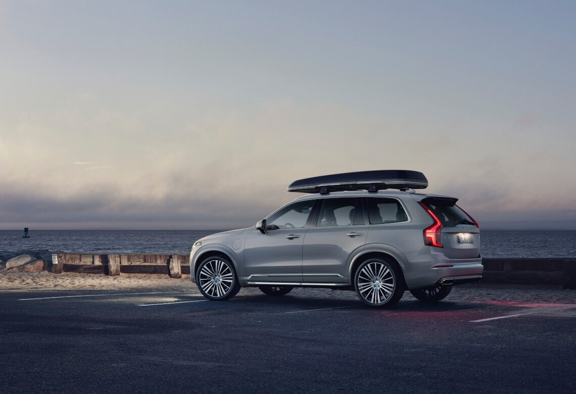 Der Volvo XC90 Inscription in Birch Light mit Dachbox steht am Meer