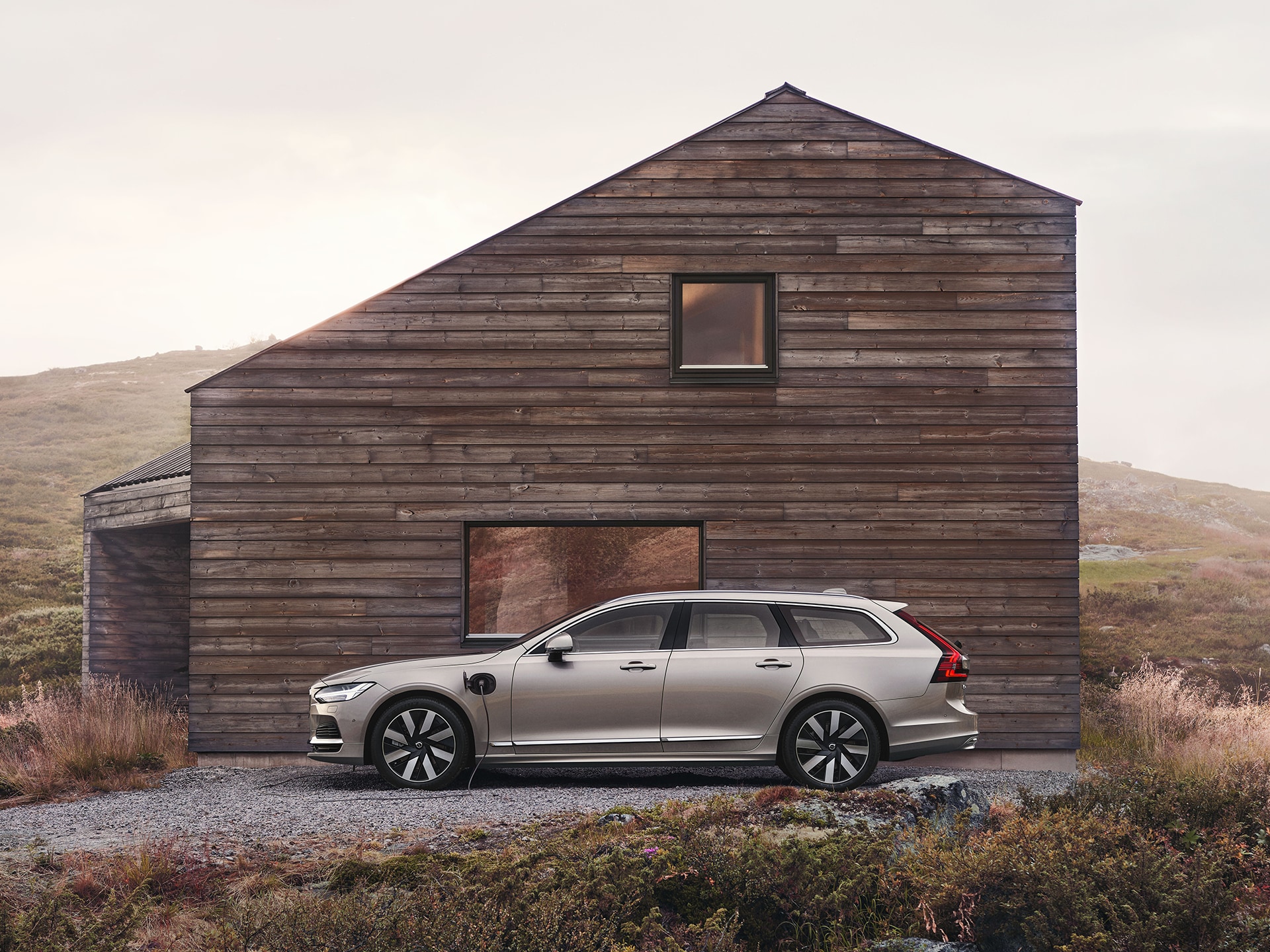 Der Volvo V90 Plug-in Hybrid vor einem Holzhaus.