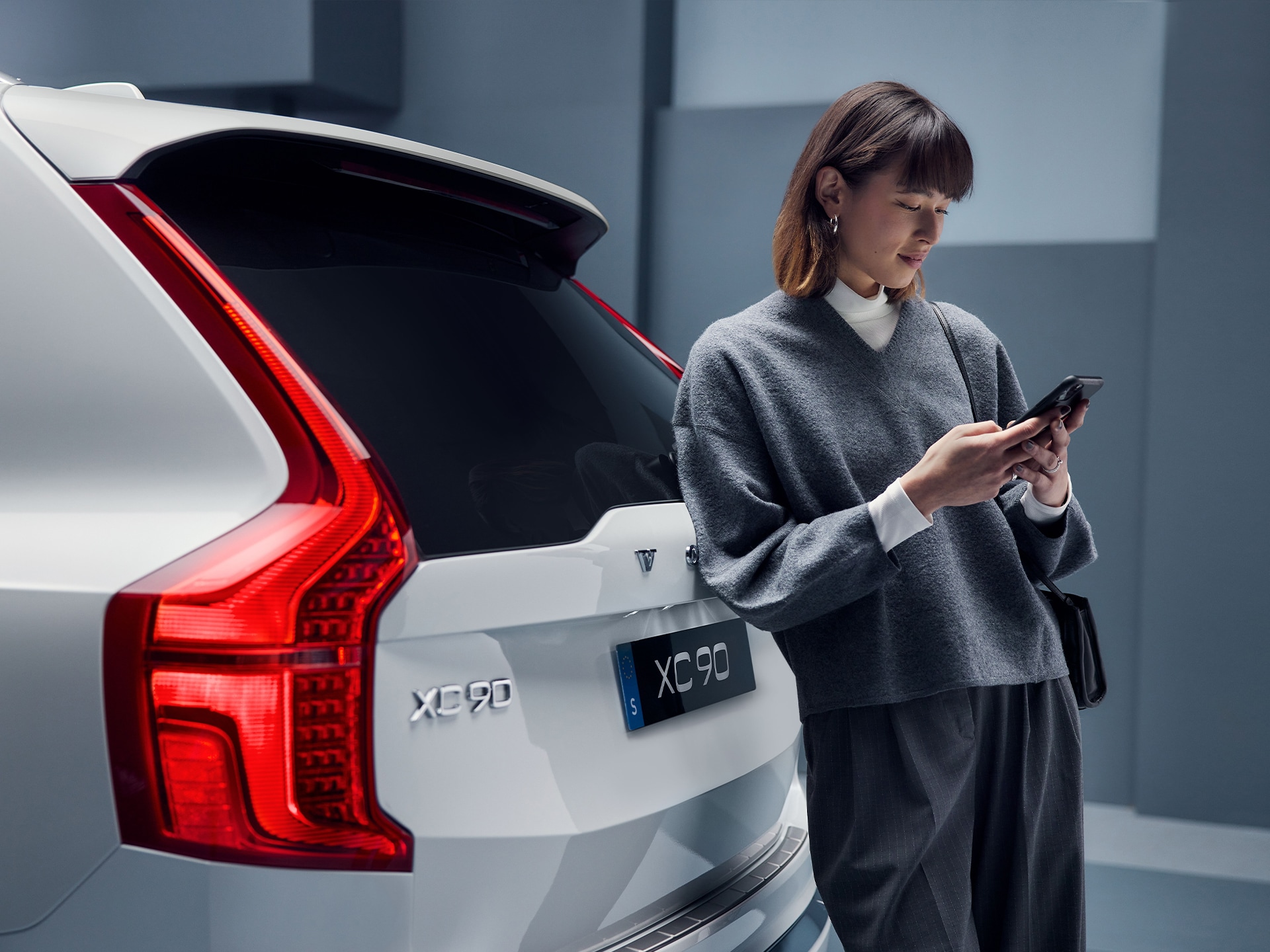 Frau steht vor einem Volvo XC90 und schaut auf ihr Smartphone