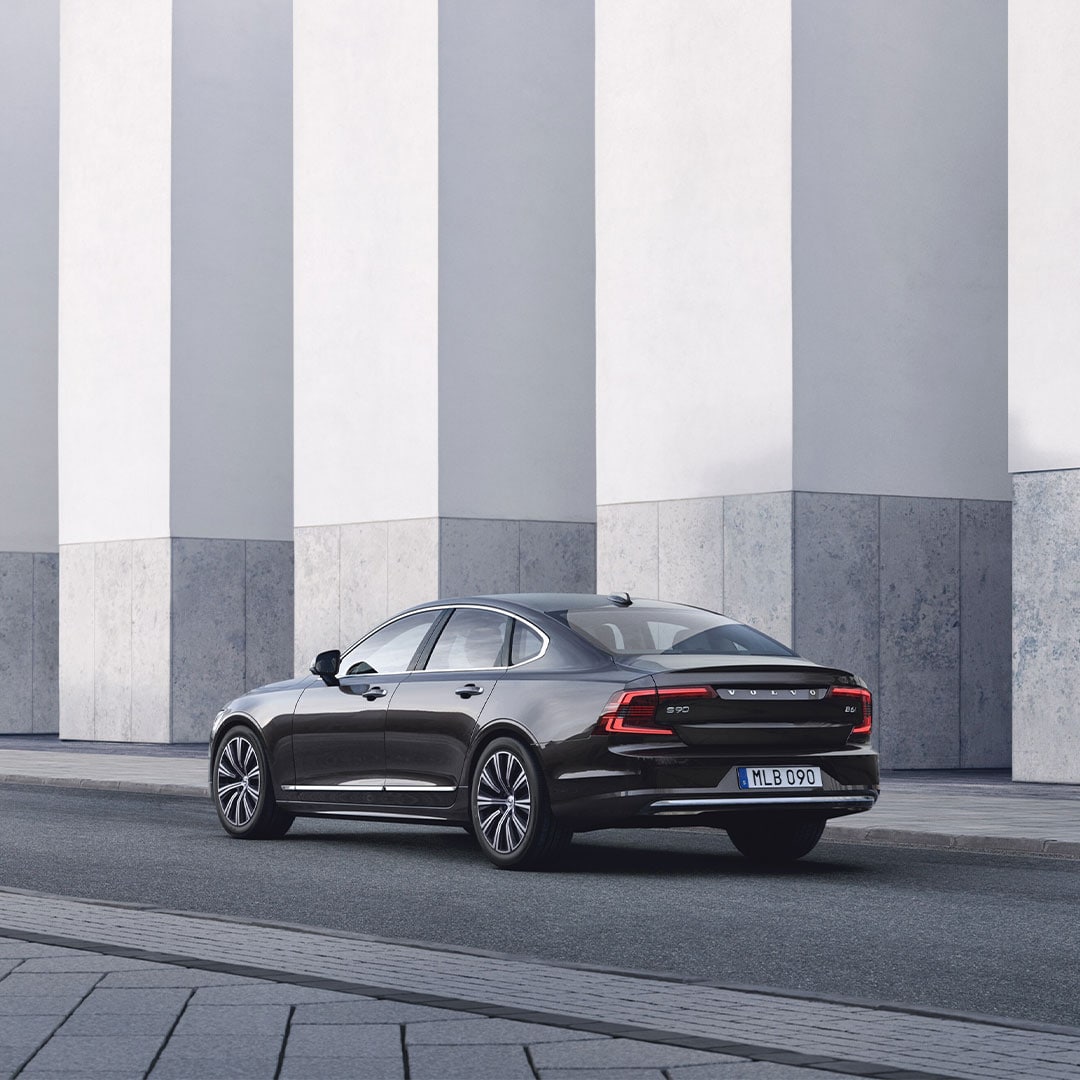 Volvo S90 seen from rear side parked in front of concrete wall.