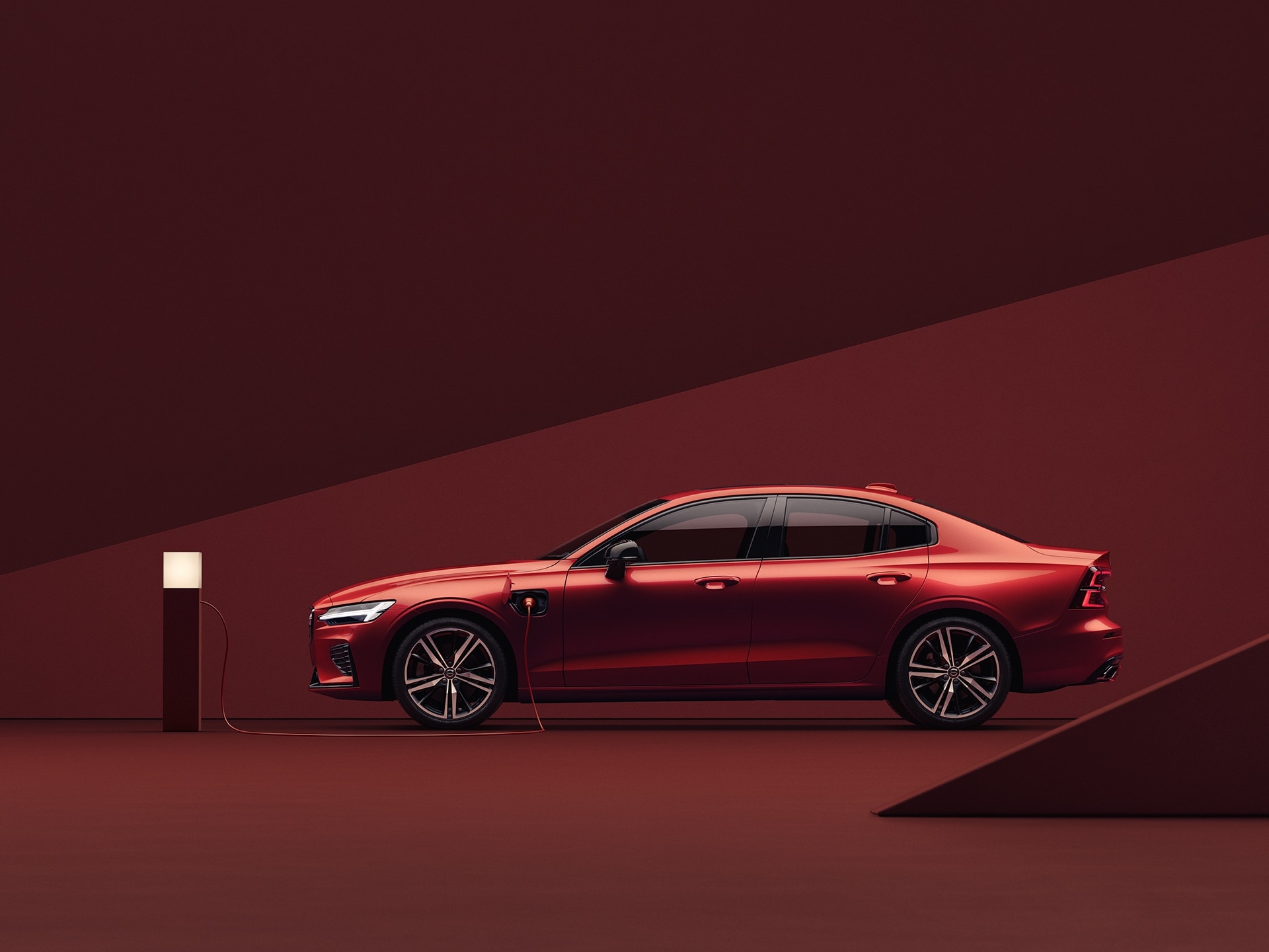 A red Volvo S60 Recharge, charging in red surroundings.